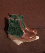 Botas de cuero marrón con la caña recubierta de corderito verde. Presentan una suela de plataforma tipo track en color beige y un tirador en la parte posterior para facilitar el calce.