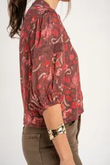 Blusa de viscosa color marrón con estampado floral en tonos rosados y rojos, de corte oversize, cuello en V con detalles de encaje y mangas largas abullonadas con inserciones de encaje.
