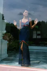 Vestido largo azul marino con tirantes anchos, escote en V y detalles de volantes rojos en el busto y la cintura. La falda es ajustada hasta la rodilla y luego se abre en una capa de tela transparente hasta el tobillo.