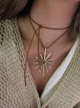 Collar con colgante dorado en forma de sol y tira de cuero sintético marrón.
