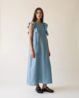 Vestido largo de lino color celeste, de calce holgado, con volados en los hombros y bolsillos delanteros aplicados.