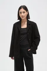 Chaqueta de gamuza sintética en color negro, con cuello solapa, cierre frontal con botones y bolsillos delanteros. Presenta un corte holgado y mangas largas.