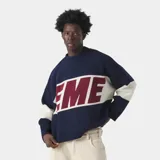 Sweater de punto grueso color azul marino con franja horizontal en el pecho que contiene la palabra "EME" en color bordó, bordeada en blanco. Las mangas son de color azul marino con una franja ancha color crema/blanco roto en la parte superior del brazo.