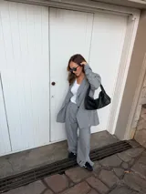 Conjunto de dos piezas compuesto por un blazer y un pantalón de corte sastrero, confeccionados en tela de algodón con estampado de rayas verticales blancas sobre fondo gris. El blazer presenta solapas clásicas y cierre frontal, mientras que el pantalón es de tiro medio y pierna recta.