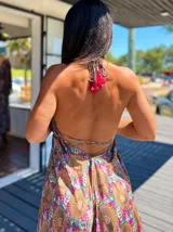 Vestido largo tipo solera, con escote en V y tirantes finos, confeccionado en seda estampada con motivos florales y patrones geométricos en tonos azules, naranjas y morados. Presenta un corte amplio y volados en el ruedo.