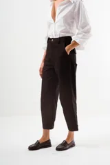 Pantalón de vestir color marrón oscuro, tiro alto, con corte recto y holgado, y puños doblados.