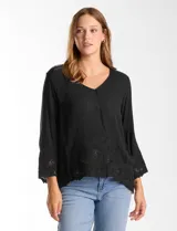 Blusa de rayón color marrón con escote en V, mangas tres cuartos acampanadas y ruedo asimétrico. Presenta detalles de bordado suizo y calados florales en puños y ruedo, con terminación festoneada.