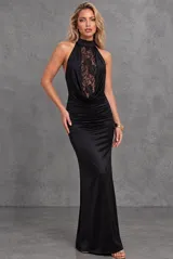 Vestido largo de fiesta color negro, con cuello halter alto y detalle de panel frontal de encaje transparente. Presenta diseño drapeado en el escote y la cintura, corte ajustado al cuerpo y espalda descubierta.