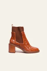 Bota corta de cuero color suela con diseño trenzado artesanal en toda la capellada. Presenta paneles laterales elásticos en color marrón oscuro y taco cuadrado de altura media.