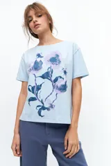 Remera celeste de algodón con estampado de flores en tonos violeta y azul. Tiene cuello redondo y mangas cortas.