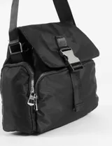 Bandolera de nylon color beige, con solapa frontal asegurada por una hebilla de clip. Cuenta con correa ajustable, bolsillos laterales con cierre y compartimento principal con cierre.