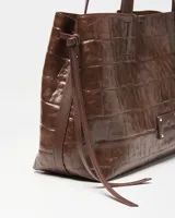 Cartera de mano tipo tote color marrón con textura símil cocodrilo, doble asa de hombro y detalles de tiras colgantes en los laterales.