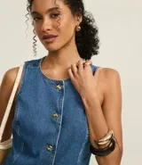 Chaleco de jeans azul oscuro, sin mangas, con cuello redondo y cierre frontal de botones blancos. Presenta un corte ligeramente alargado y solapas frontales que simulan bolsillos.