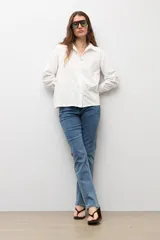 Camisa blanca de manga larga con frente de tela broderie con diseño de rombos calados y espalda lisa. Presenta cuello clásico y cierre frontal con botones.