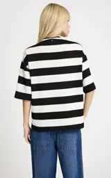 Blusa de punto con estampado de rayas horizontales en blanco y negro. Presenta un corte holgado, cuello redondo con panel frontal sólido en contraste, cierre de cremallera metálica, mangas cortas anchas y un parche bordado en la manga derecha.