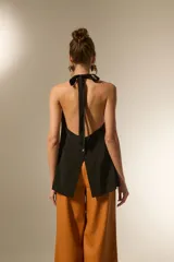 Chaleco largo negro, con escote halter y abertura frontal con botones joya. Corte entallado en la parte superior y ligeramente acampanado en el bajo.