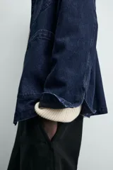 Chaqueta de denim de algodón en color azul oscuro con corte relaxed fit. Presenta cuello de solapa, cierre frontal con botones metálicos y tres bolsillos de parche en el delantero. Las mangas son largas con puños abotonados.