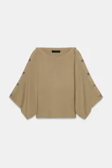 Jersey de punto color beige con cuello barco y mangas anchas tipo capa que presentan detalle de botones a lo largo de los hombros y brazos.