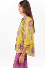 Camisa de manga larga con cuello clásico y cierre frontal de botones, confeccionada en tejido de color verde lima con estampa floral en tonos morados y naranjas.