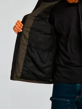 Chaleco acolchado bicolor con diseño de bloques en negro y verde oliva. Presenta cierre frontal completo, cuello alto, bolsillos laterales con cierre y logo de la marca estampado en el pecho.