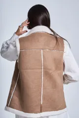 Chaleco símil cuero color marrón, con interior de corderoy color crema, cuello solapa y cierre frontal con cremallera.