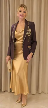 Blazer de gamuza color tostado con diseño artesanal. Presenta flecos en las solapas y bolsillos, bordados florales en los hombros con detalles de perlas colgantes y aplicaciones decorativas en los bolsillos.