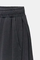 Pantalón de algodón color beige con tiro medio, cintura elástica ajustable con cordón y perneras anchas con pliegues delanteros y bolsillos laterales.