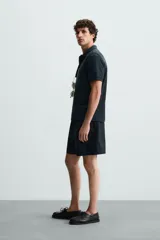 Polo de manga corta color blanco roto, con cuello solapa y cierre frontal de cremallera. Presenta un tejido de piqué estructurado y corte regular fit.