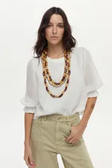 Blusa de lino blanca con escote redondo y mangas cortas abullonadas con detalles de volados en los puños.