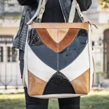 Bolso tipo tote de cuero vacuno color tostado, natural y negro, con diseño geométrico. Tiene manija corta y correa ajustable y removible para usar como morral. Cuenta con dos bolsillos verticales externos, forro interior, bolsillo interno con cierre y bolsillo pequeño para el móvil.