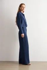 Pantalón de corte recto y tiro medio, confeccionado en tejido negro de textura sutil. Presenta un diseño minimalista con cierre frontal oculto y caída fluida.