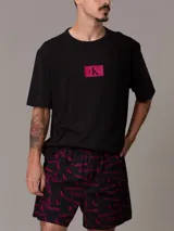 Conjunto de pijama Calvin Klein 1996, compuesto por una remera negra de algodón con cuello redondo, manga corta y logo estampado en el pecho, y un short negro de algodón tejido con bolsillos laterales, cintura elástica con logo y estampado del logo de la marca en color fucsia.