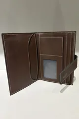 Billetera viajera de cuero color chocolate, con costuras blancas a la vista y cierre mediante solapa con broche.