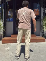 Remera verde militar de corte oversize con cuello redondo y estampado en la espalda con el logo de Brixton, una flor de hibisco y la frase "Where hibiscus grows, peace flows".