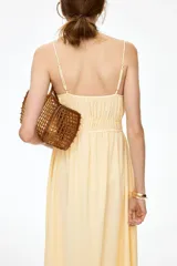 Vestido midi de algodón con textura efecto arrugado, color amarillo, tirantes finos ajustables, escote corazón con abertura tipo cerradura y lazo frontal, cintura elástica fruncida y falda evasé con vuelo ligero.