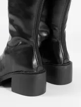 Bota bucanera de caña alta hasta la rodilla, confeccionada en cuero sintético negro. Presenta una estructura firme, cierre lateral y un taco bloque con plataforma integrada.