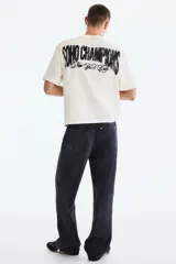 Remera de algodón en color blanco, de corte holgado, con cuello redondo acanalado, mangas cortas y hombros caídos. Presenta un pequeño estampado en el pecho con la inscripción "SOHO CHAMPIONS New York City".