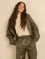 Chaqueta bomber de eco cuero color verde oliva, con cuello tipo solapa, cierre frontal metálico, bolsillos laterales y puños elásticos.