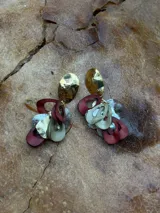 Par de aros colgantes con base dorada y formas abstractas en color borgoña, plateado y beige.