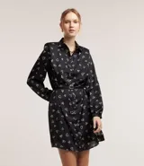 Vestido corto modelo chemise, color negro con estampado de corazones blancos, de manga larga abullonada con hombreras y puños ajustados. Incluye cinturón para lazo en la cintura.