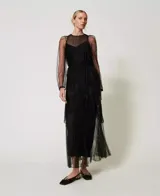 Vestido largo de tul negro con volantes plisados e inserciones de encaje. Presenta un escote redondo con lágrima, manga larga transparente, cremallera invisible lateral, cinturón fino de la misma tela y combinación, de corte ancho.