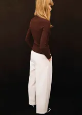 Pantalón de vestir color crudo, de corte recto y largo, con pliegues en los laterales y cierre delantero de cremallera metálica expuesta.