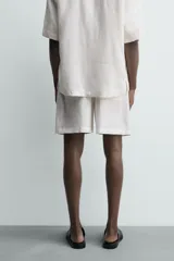 Bermuda de lino color blanco hueso, de corte relajado y tiro medio. Presenta cintura elástica ajustable con cordón, pliegues frontales y bolsillos laterales y trasero.