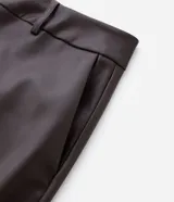 Pantalón de cuero sintético con corte barrel, de tiro alto y pierna ancha con estructura curva. Presenta bolsillos laterales tipo cuchillo y costuras decorativas con pespuntes visibles.