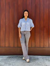 Camisa de corte recto y calce holgado, confeccionada en tela liviana color celeste con estampado de rayas verticales blancas con detalles de hojas. Presenta cuello en V, cierre frontal con botones de madera y mangas tres cuartos con terminación elástica.