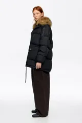 Campera tipo plumífero de largo medio y corte recto en tejido técnico, con cierre frontal, capucha con borde de pelo sintético desmontable y bolsillos frontales con solapa.