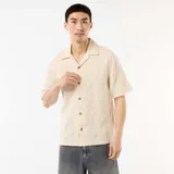Camisa de manga corta color beige con cuello tipo campamento, cierre frontal de botones y diseño de textura en punto fantasía.