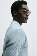 Polo de manga corta, color celeste pálido, con cuello solapa y abertura frontal en V. Tejido de punto con textura acanalada vertical.