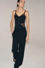 Body de escote corazón con aros y tirantes finos ajustables. Presenta un diseño con paneles de tejido opaco y transparencias laterales. Cierre inferior con botones a presión.