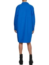 Vestido camisero de corte oversize confeccionado en algodón orgánico. Presenta cuello inglés, cierre frontal de botones, mangas largas con puños abotonados y largo hasta la rodilla. Incluye el logo de la marca bordado en uno de los puños.